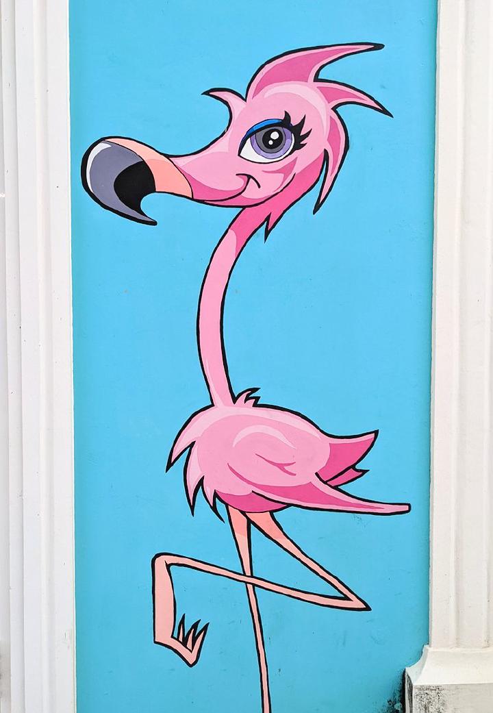 A flamingo painted on a wall with more of a cartoony style with big pretty eyes and the classic standing on one leg pose.