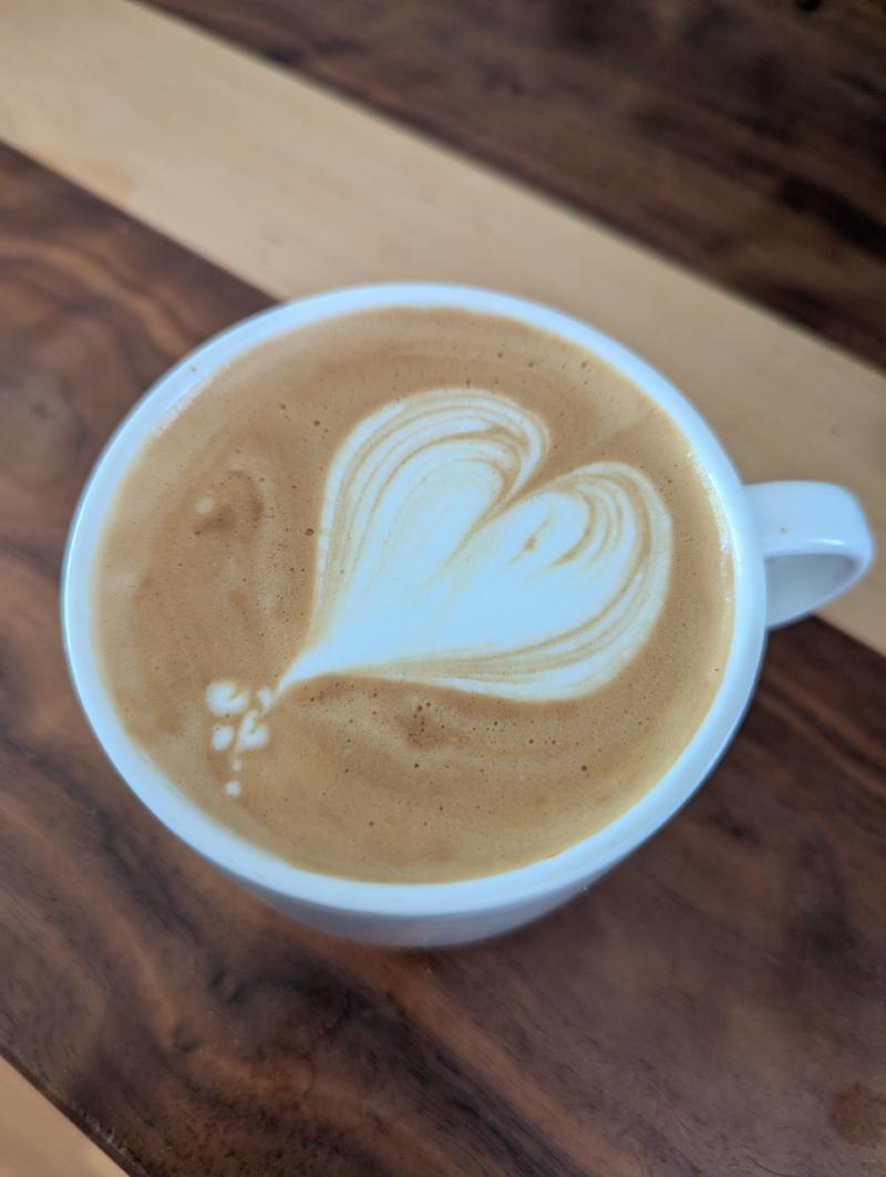 A white coffee cup on a dark walnut wooden table top with some latte 'art' somewhere between and onion and a heart