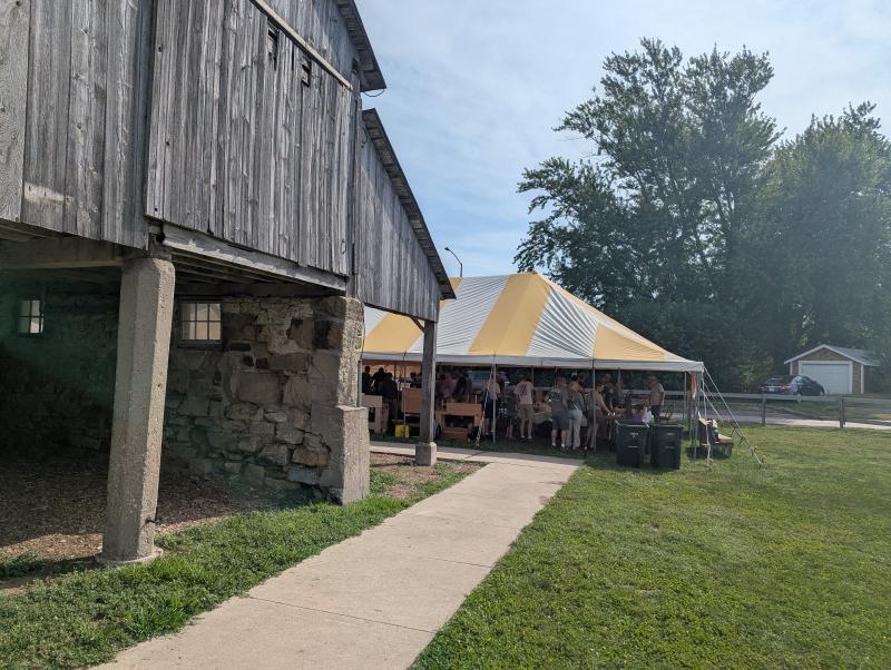 Old barn with a yellow and white tent beyond.