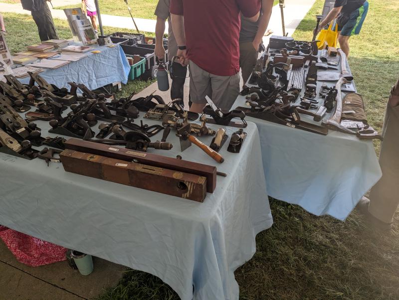 Old woodworking tools for sale on table tops and people browsing
