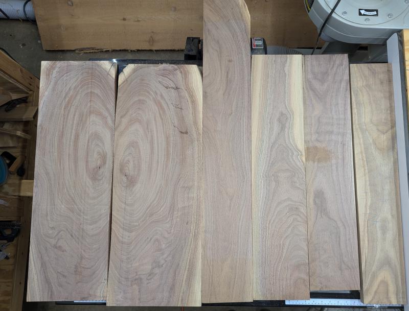 Six boards of walnut are laid on top of a table saw, there's of differing lengths and widths.